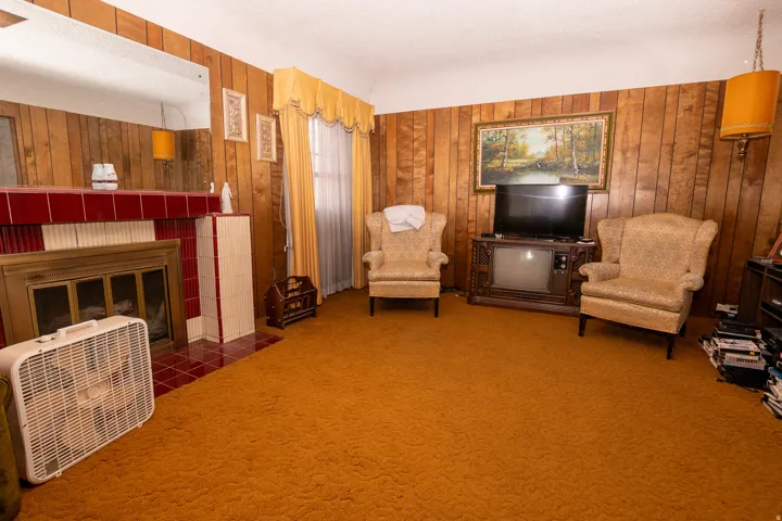 Living area featuring a tile fireplace, wooden walls, heating unit, a textured ceiling, and carpet