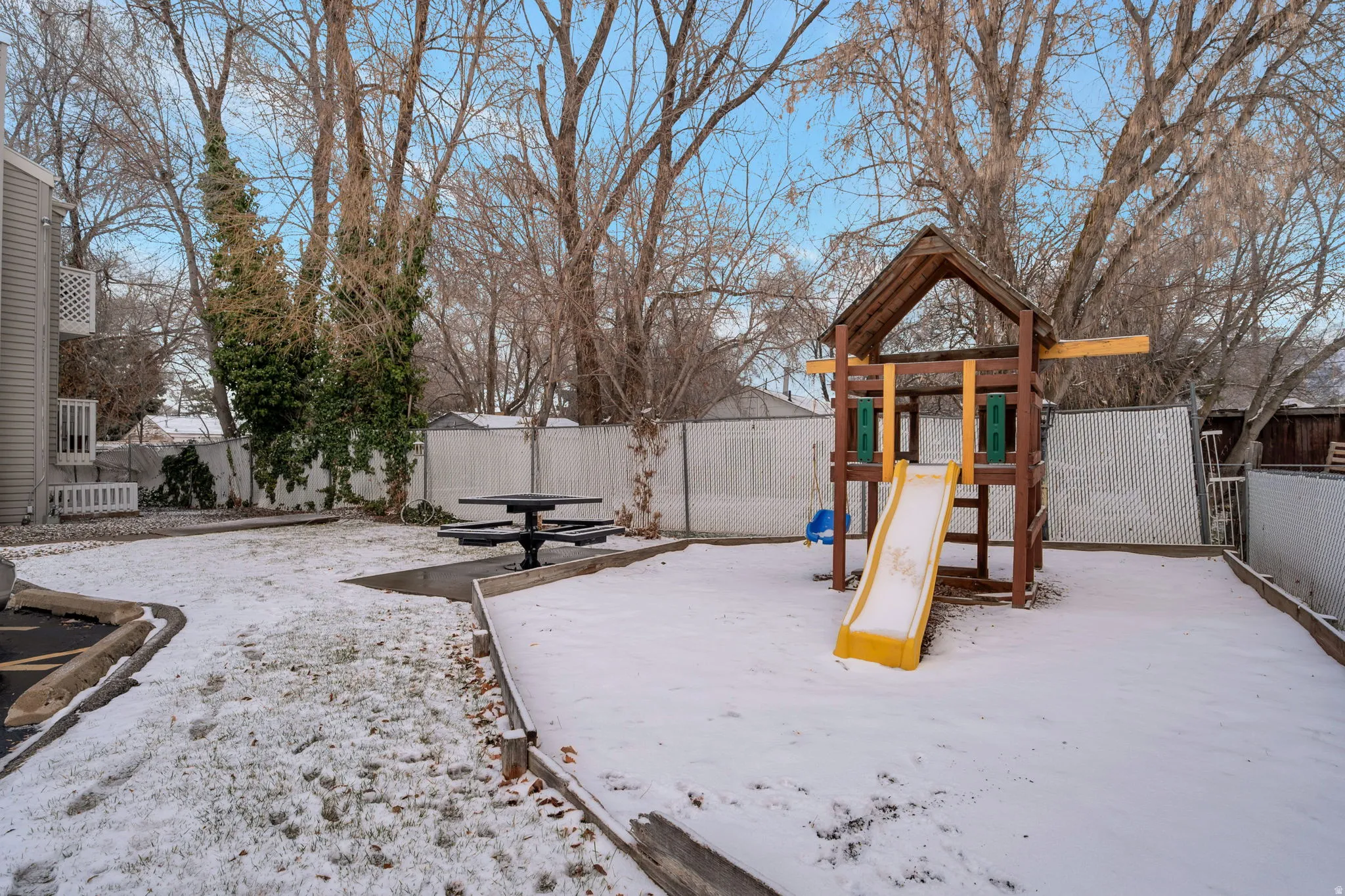 Snow covered playground featuring a fenced backyard and a playground