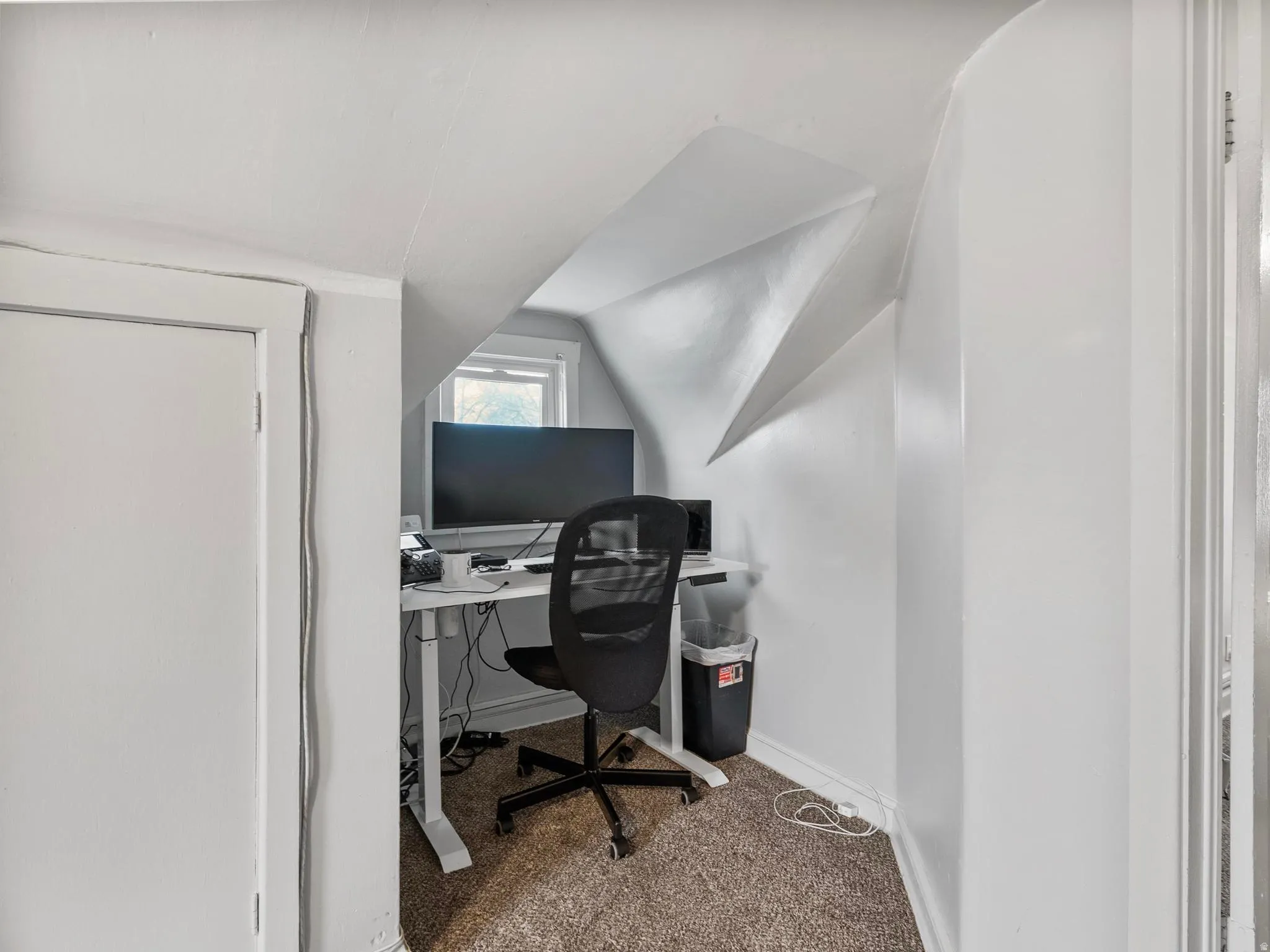 Carpeted office space featuring baseboards and vaulted ceiling