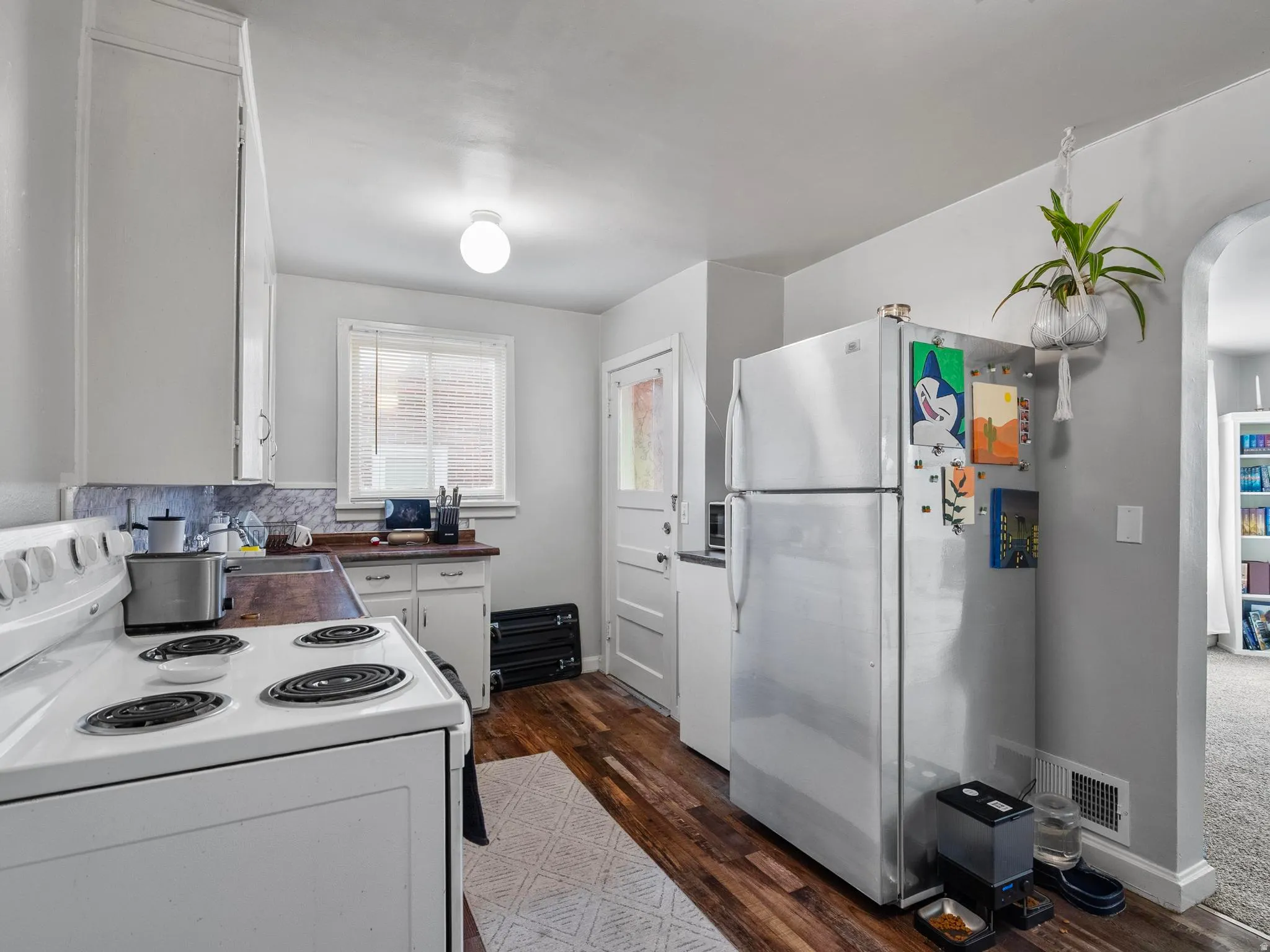 Kitchen with white appliances, white cabinets, dark wood finished floors, and arched walkways
