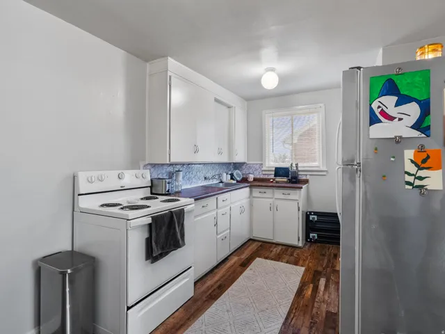 Kitchen featuring white electric range, freestanding refrigerator, dark wood-style flooring, white cabinetry, and decorative backsplash