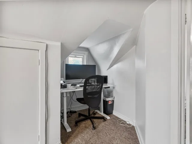 Carpeted office space featuring baseboards and vaulted ceiling