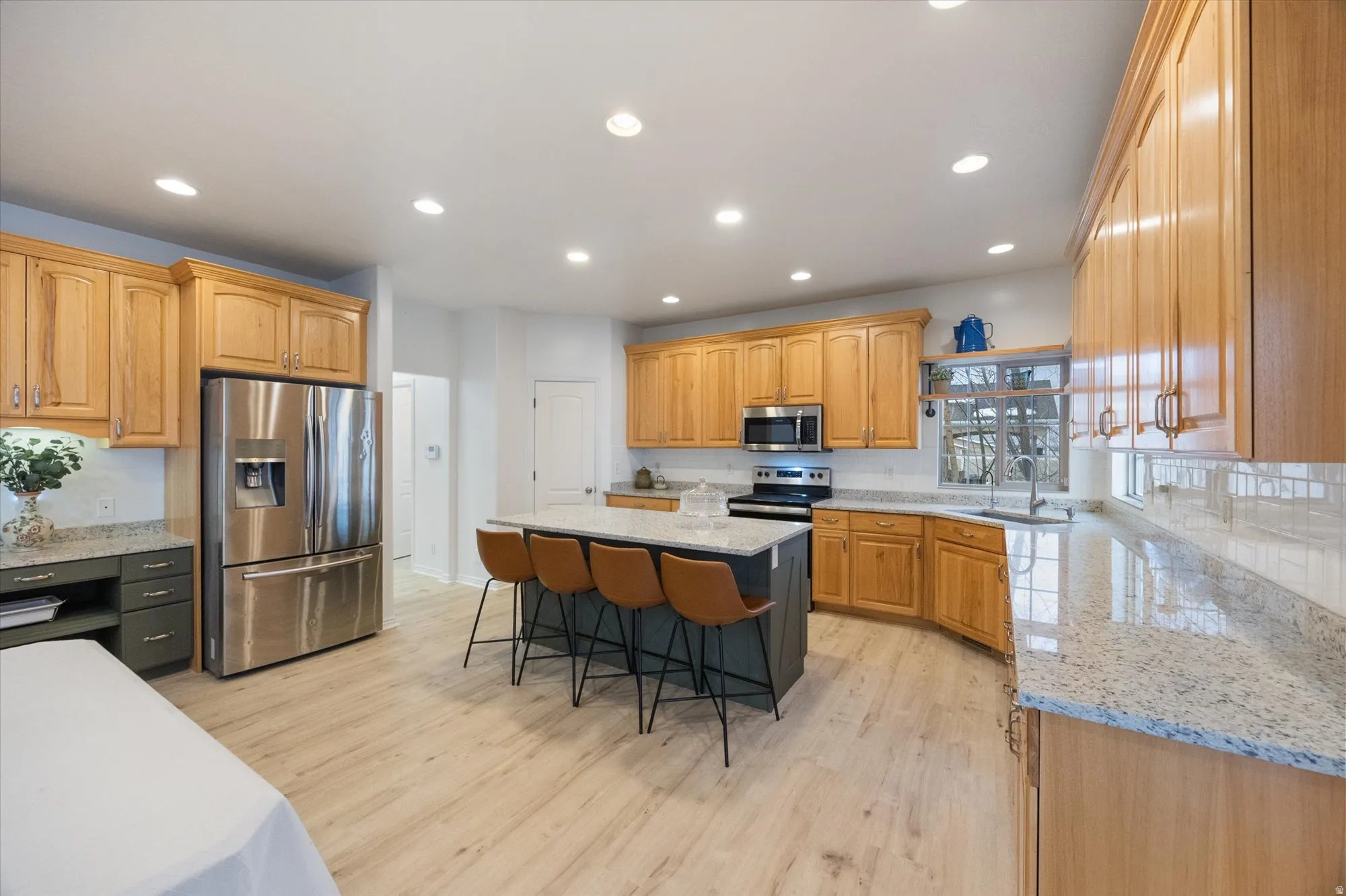 Kitchen with light stone countertops, stainless steel appliances, a kitchen island, a breakfast bar area, and light wood-type flooring