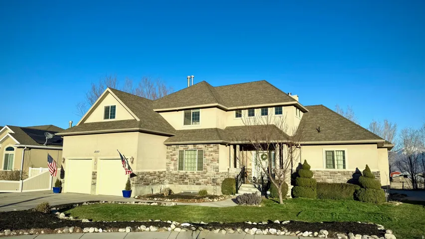 View of front of property featuring stucco siding, roof with shingles, stone siding, and driveway