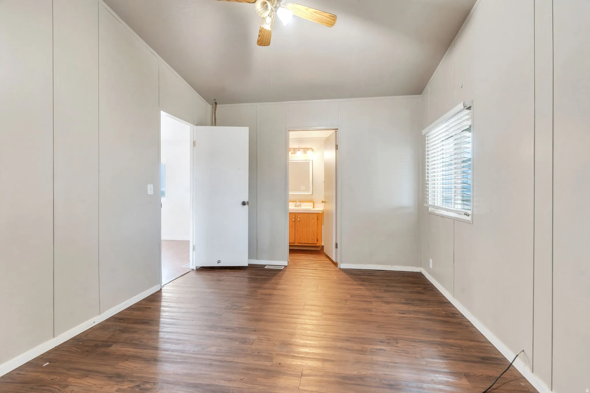 Unfurnished bedroom featuring a decorative wall, dark wood finished floors, a ceiling fan, and ensuite bathroom