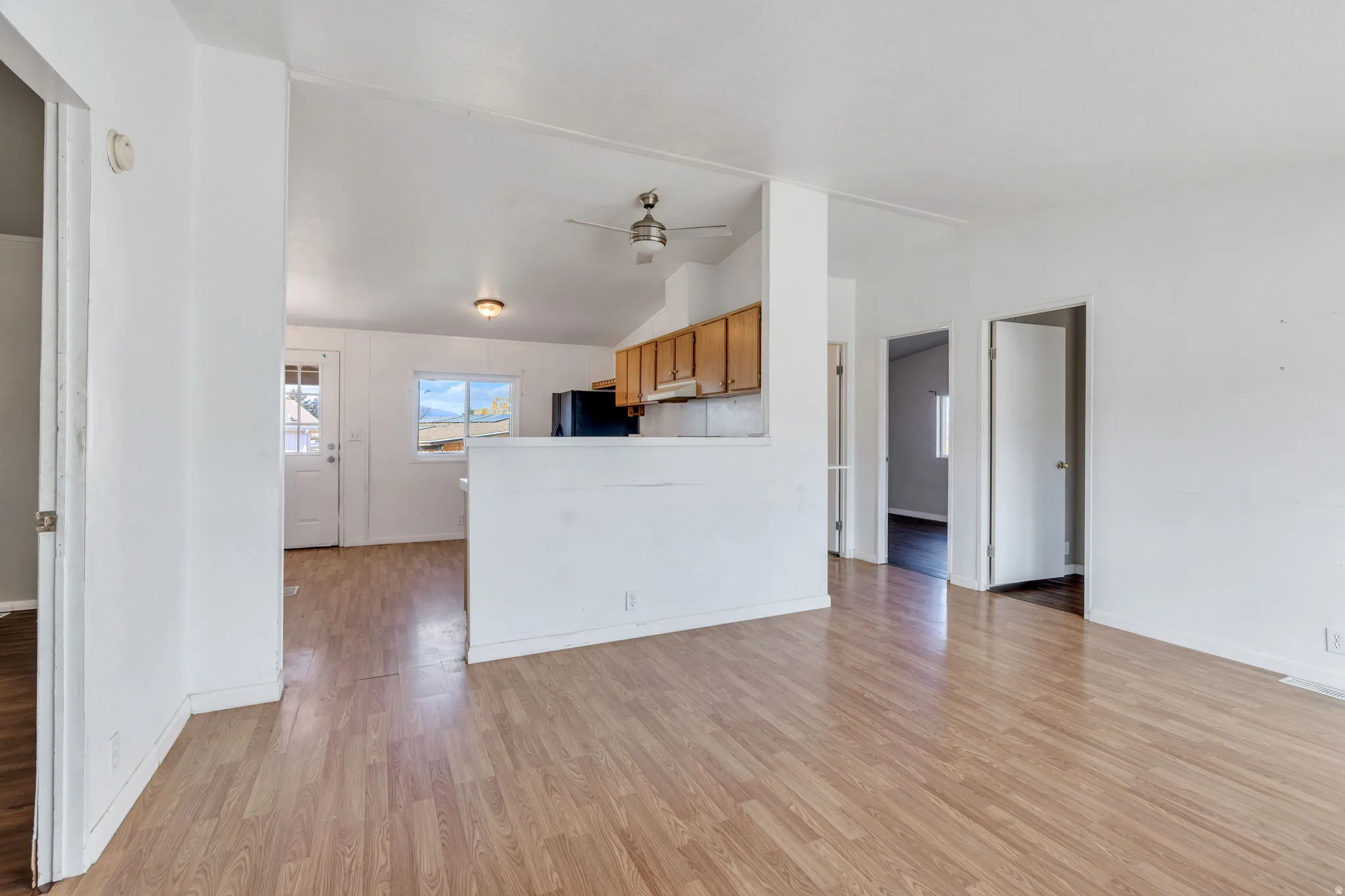 Unfurnished living room with a ceiling fan, light wood-type flooring, and vaulted ceiling