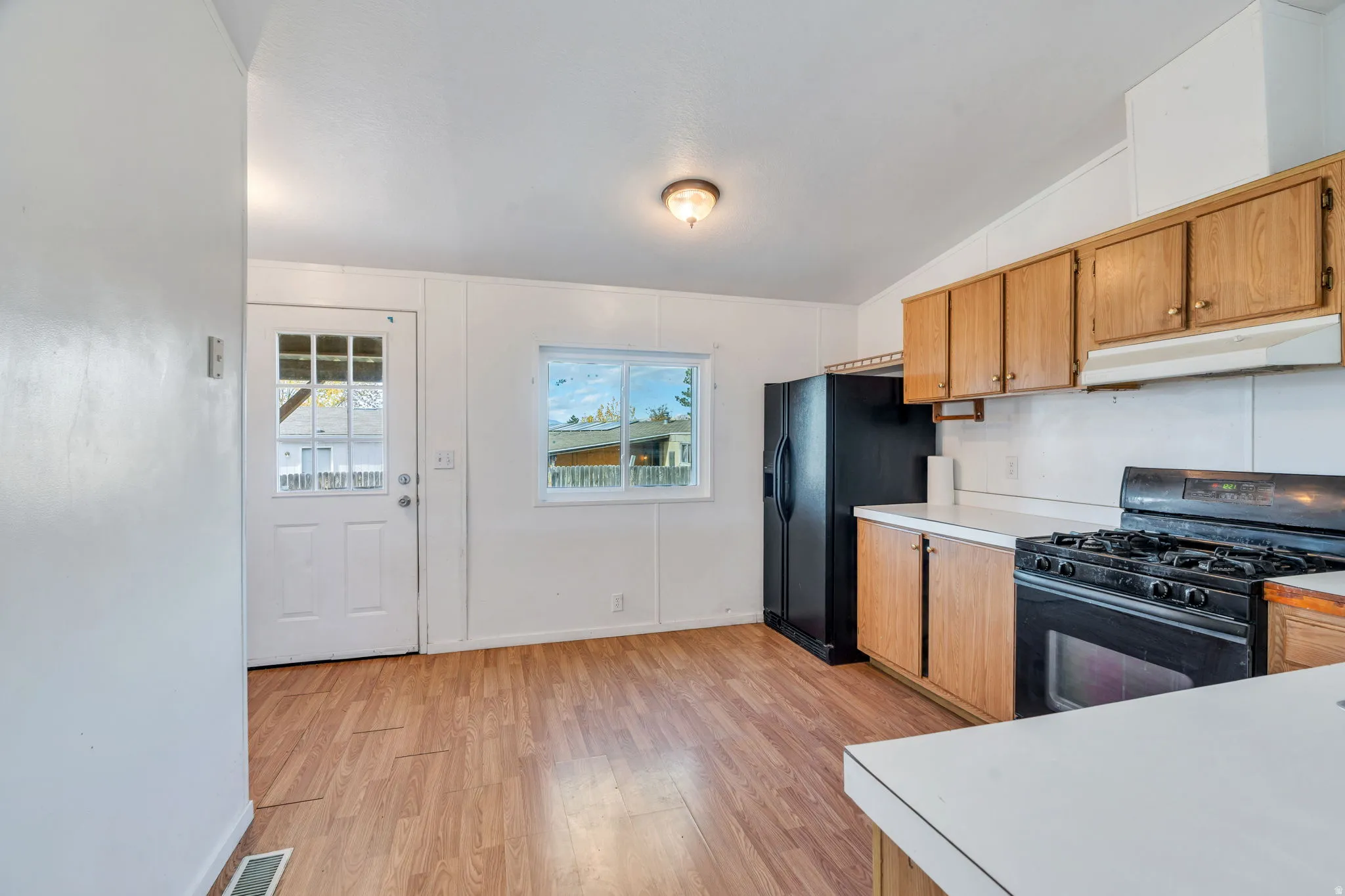 Kitchen featuring black appliances, light countertops, vaulted ceiling, light wood-type flooring, and under cabinet range hood