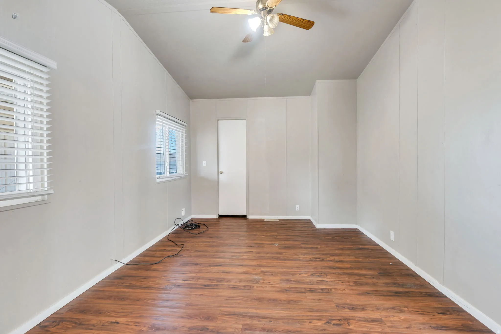 Unfurnished bedroom featuring a decorative wall, dark wood-style flooring, and a ceiling fan