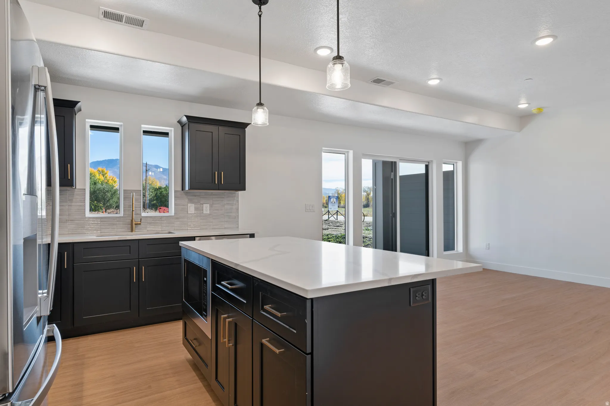 Kitchen featuring decorative backsplash, stainless steel fridge, light wood-type flooring, pendant lighting, and recessed lighting