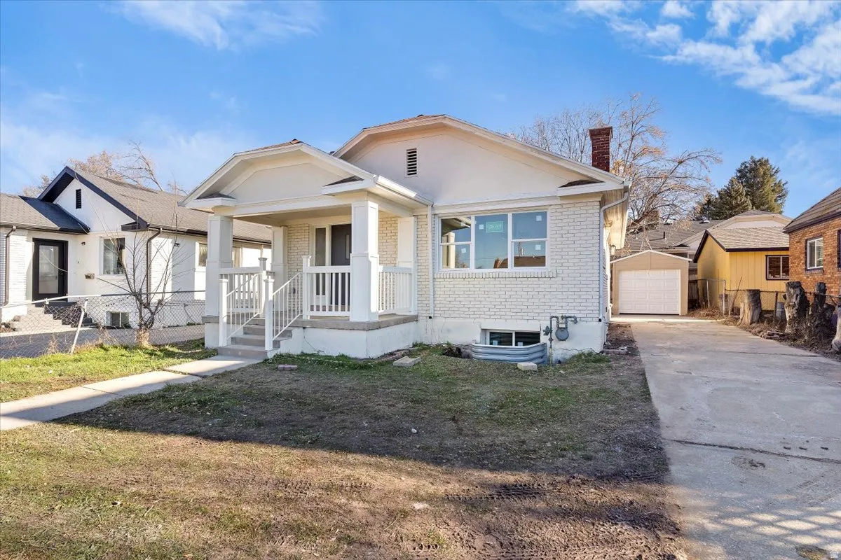 Bungalow-style home with brick siding, a chimney, an outbuilding, driveway, and a garage