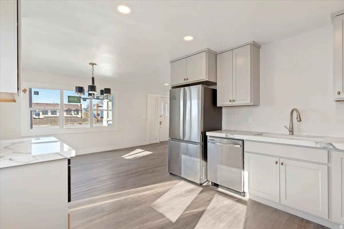 Kitchen featuring decorative light fixtures, stainless steel appliances, recessed lighting, light stone countertops, and light wood-style flooring