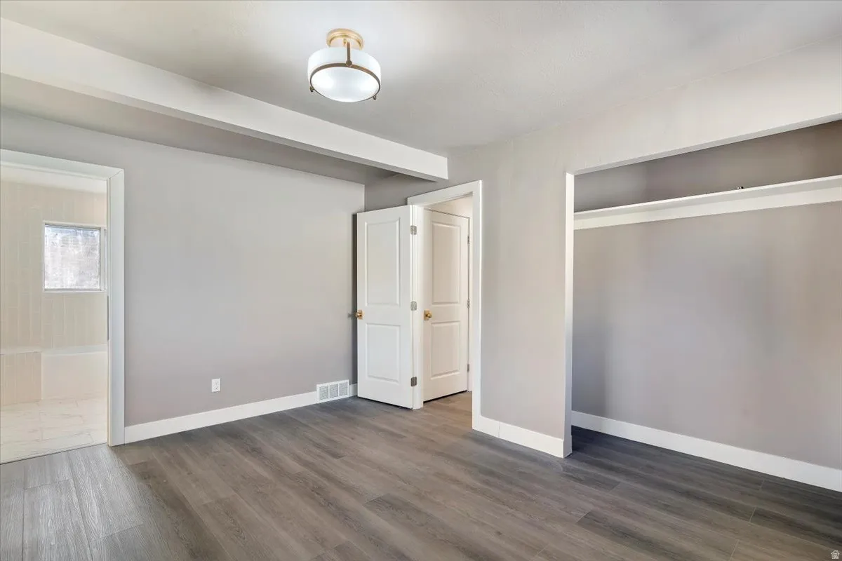 Unfurnished bedroom with dark wood-style floors, a closet, and ensuite bathroom