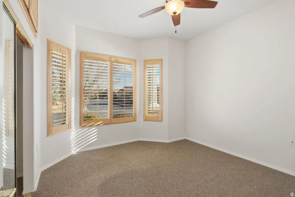 Carpeted empty room featuring a ceiling fan and baseboards