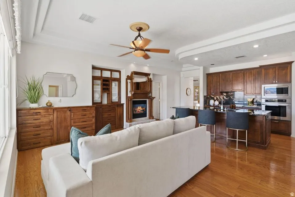 Living area featuring light wood-type flooring, ceiling fan, a glass covered fireplace, and recessed lighting