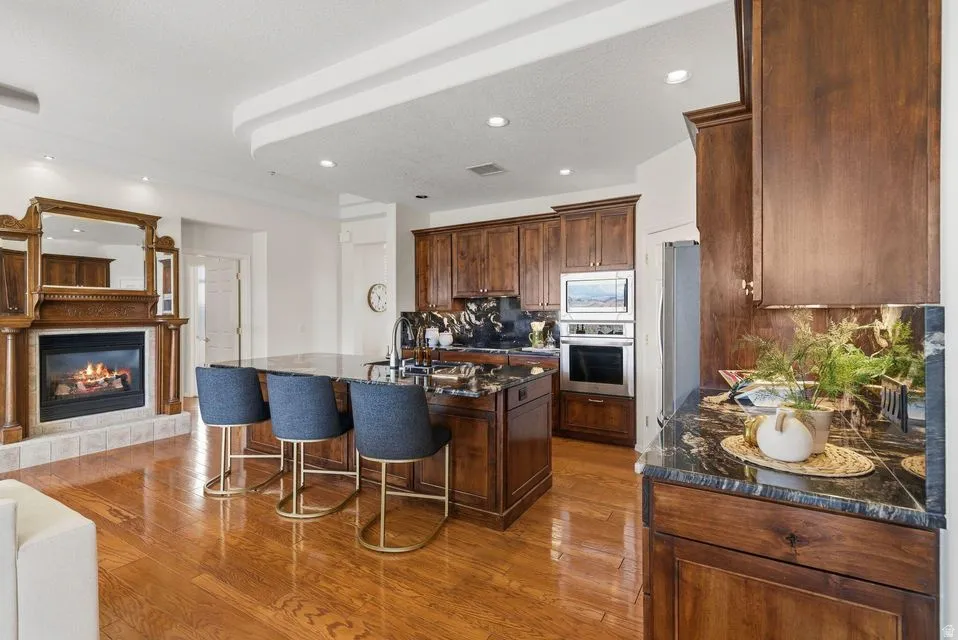 Kitchen with an island with sink, stainless steel appliances, dark stone countertops, a glass covered fireplace, and light wood-style flooring