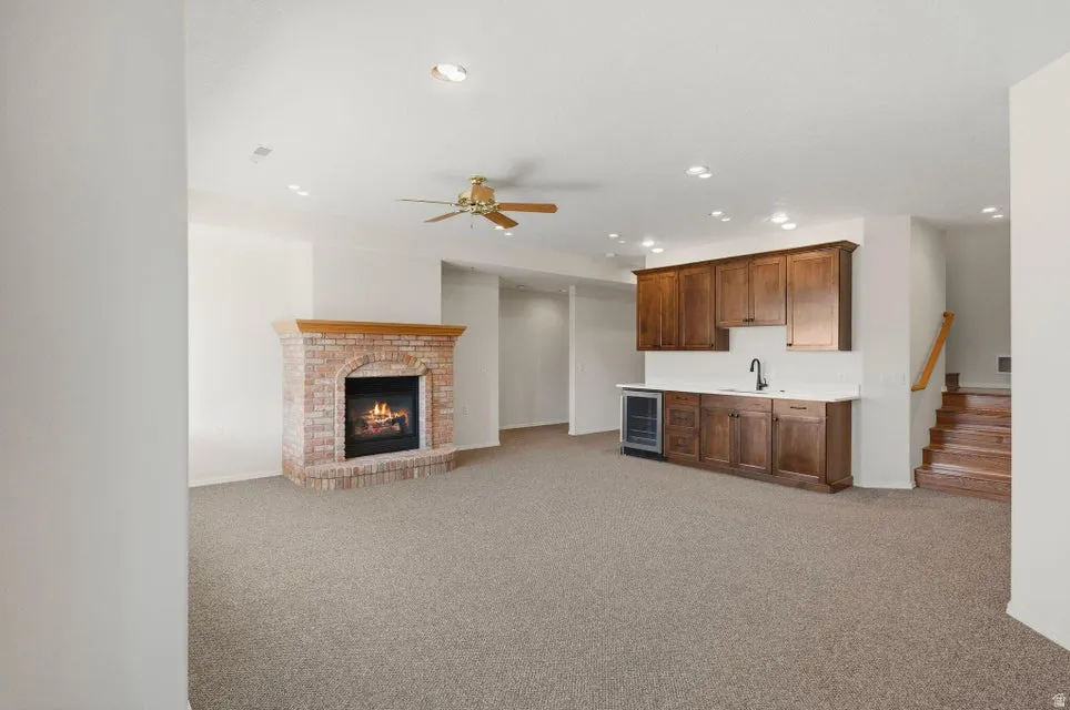 Unfurnished living room featuring light carpet, a brick fireplace, recessed lighting, wet bar, and wine cooler