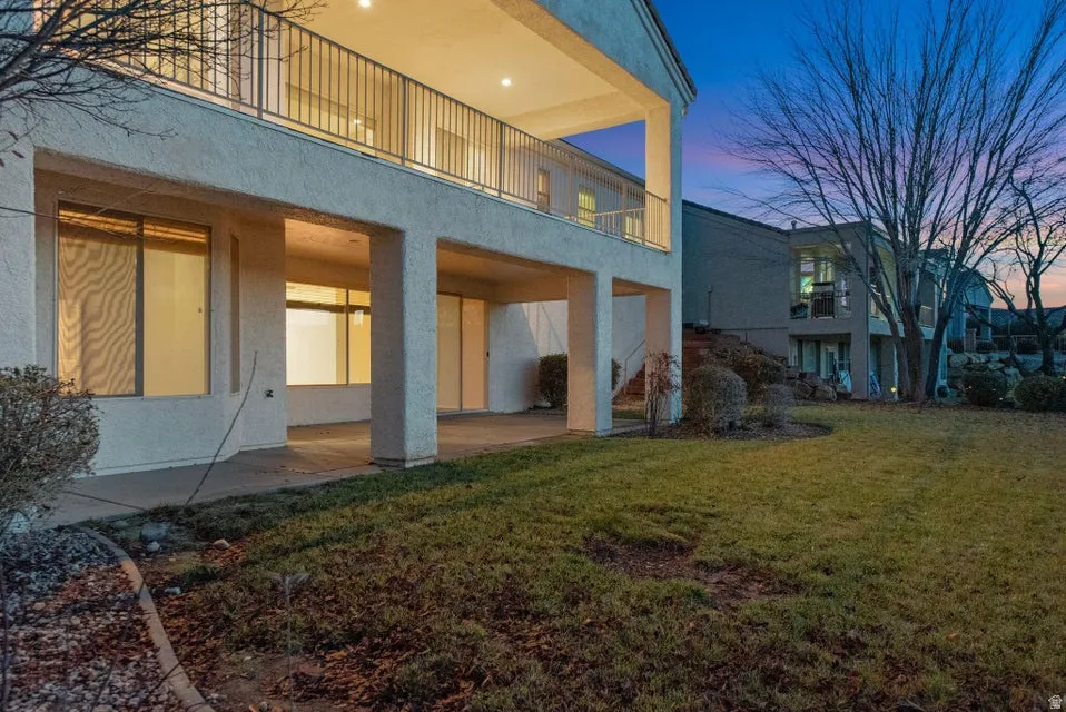 Rear view of property with a patio area, a balcony, a yard, and stucco siding