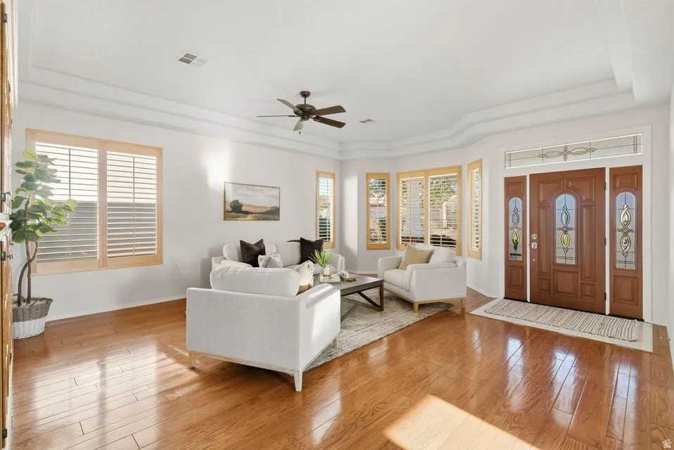 Living area with a raised ceiling, light wood-type flooring, and a ceiling fan