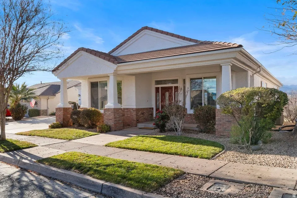 View of front of house with brick siding, covered porch, stucco siding, a tiled roof, and a front yard