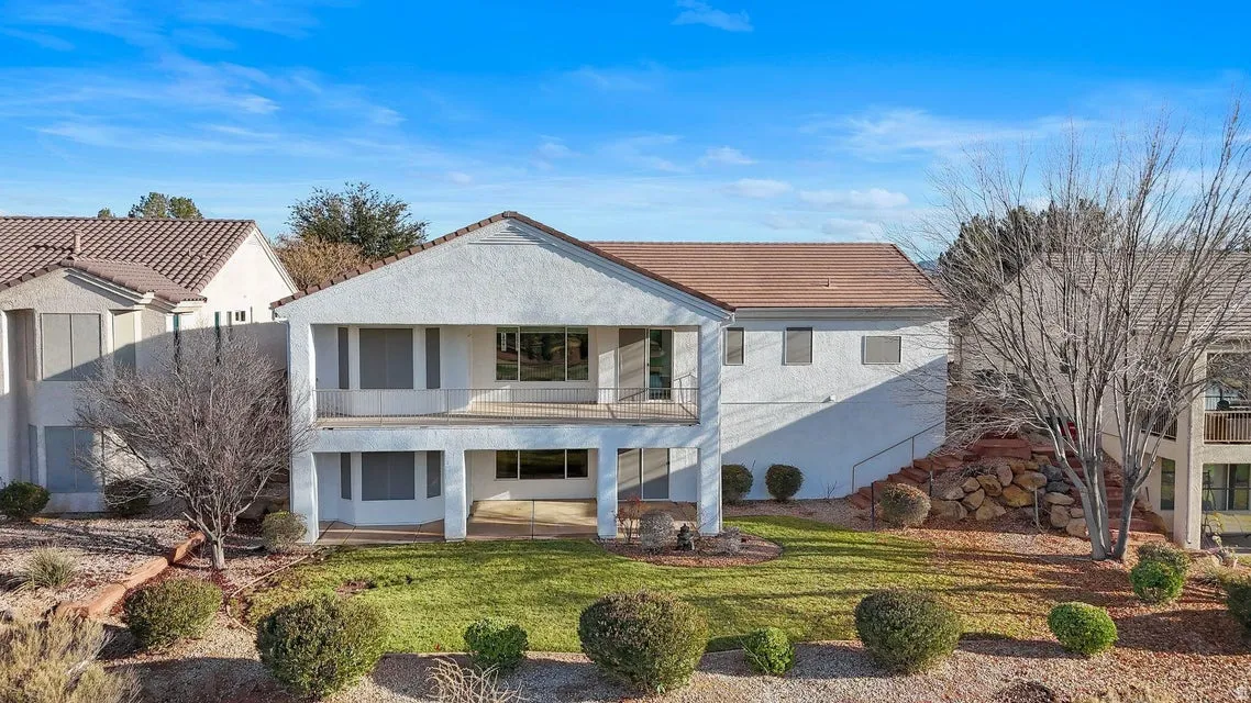 Back of house featuring a balcony, a yard, and stucco siding