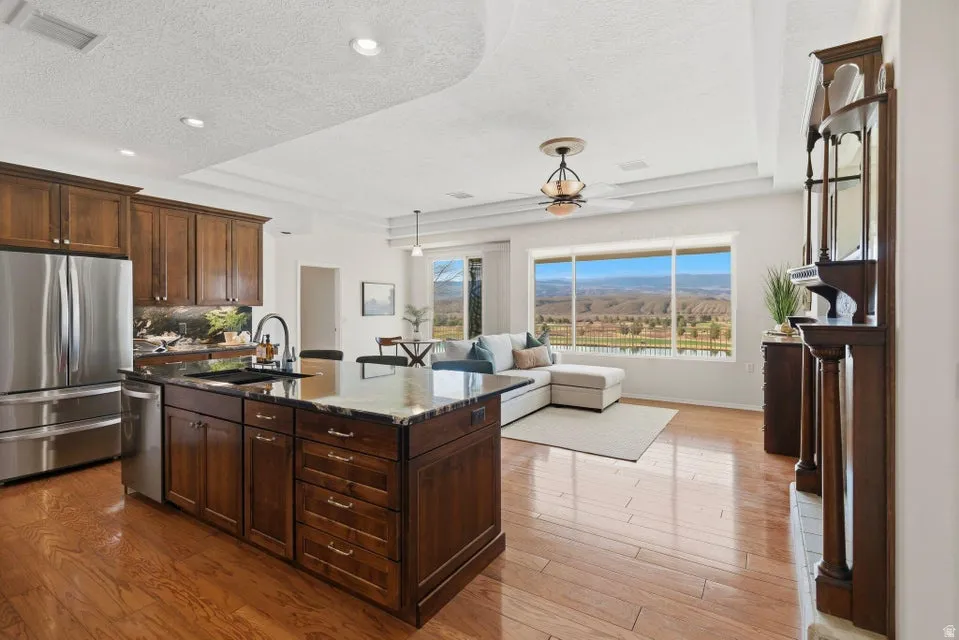 Kitchen with dark stone countertops, a tray ceiling, stainless steel appliances, a kitchen island with sink, and a textured ceiling