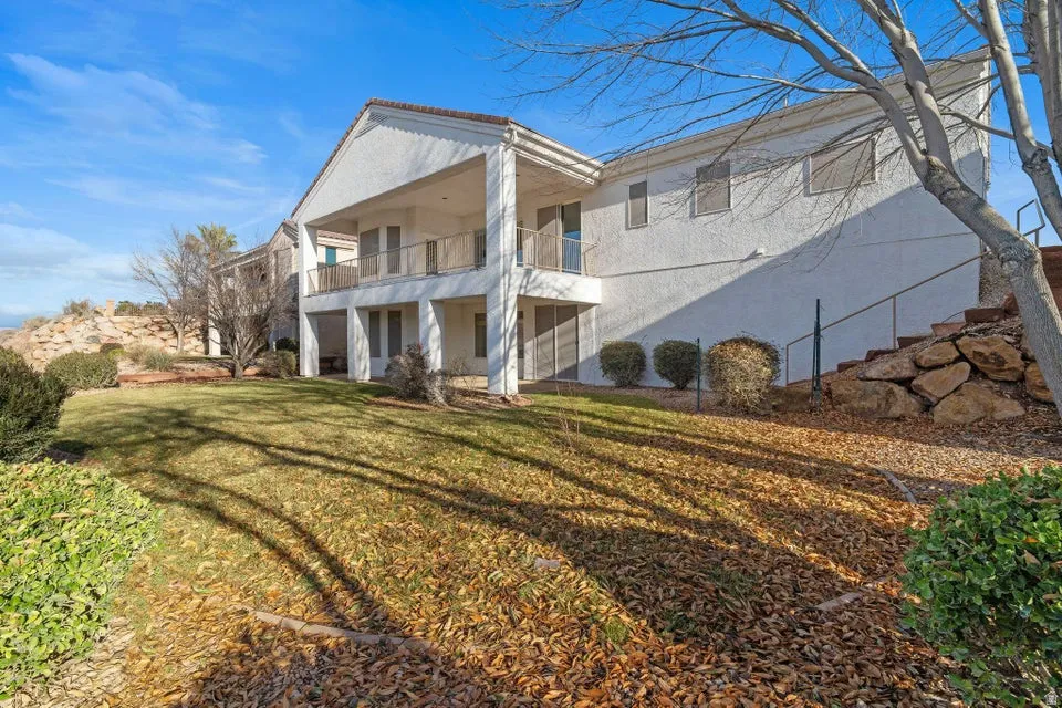 Back of property featuring a lawn, stucco siding, and a balcony