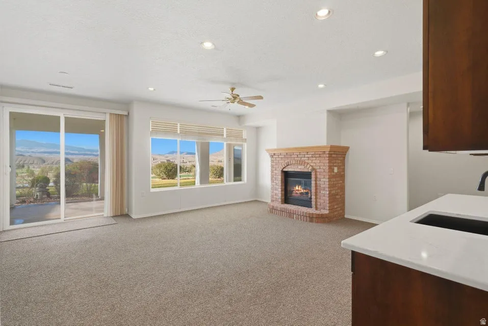 Unfurnished living room featuring a mountain view, light colored carpet, a brick fireplace, ceiling fan, and recessed lighting