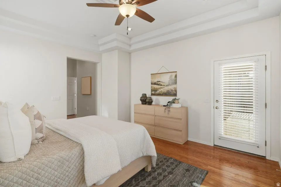 Bedroom with a raised ceiling, wood finished floors, and a ceiling fan