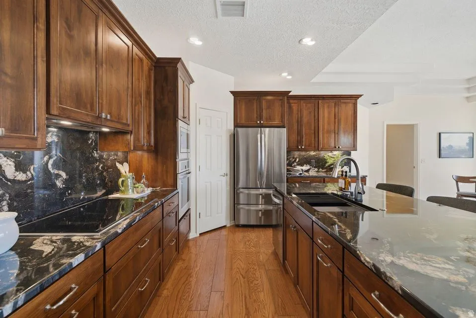 Kitchen with dark stone countertops, stainless steel appliances, light wood-style flooring, a textured ceiling, and recessed lighting