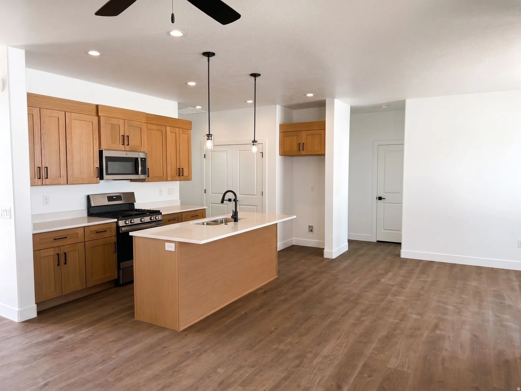 Open-concept kitchen featuring wood-finish cabinetry, stainless steel appliances, a center island with sink, and wood-finish flooring