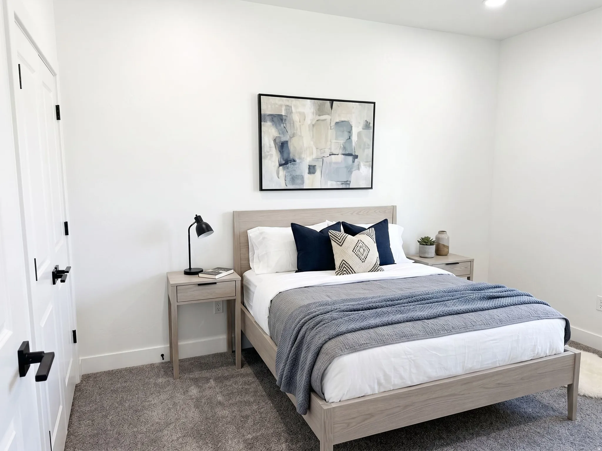 Ai Staged. Recessed ceiling lighting, white walls, gray carpeting, white paneled doors with black hardware, and light wood-finish nightstands
