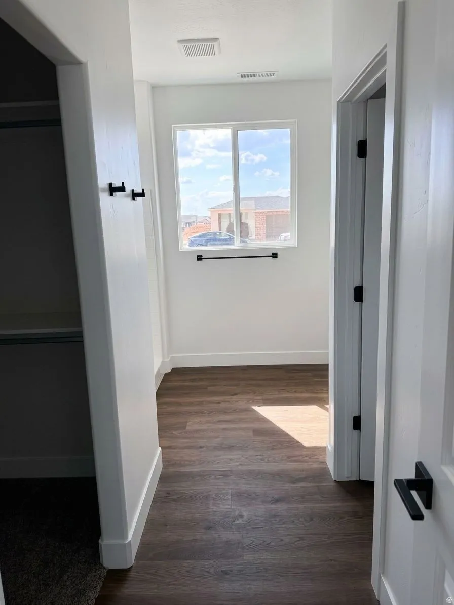 Window with black towel bar, dark wood-finish flooring, white walls, and black door hardware