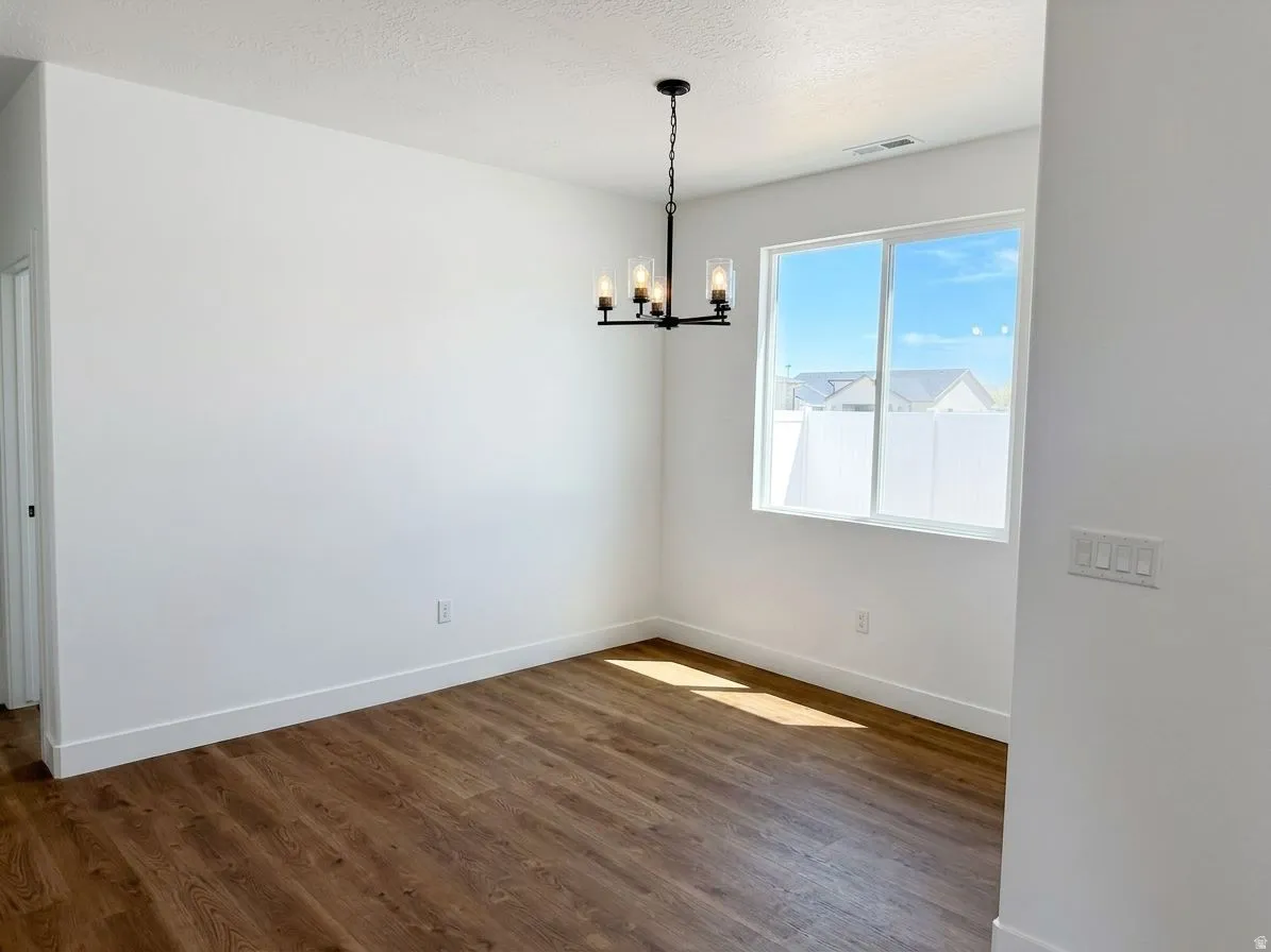 Wood-finish flooring, white walls, and a black chandelier with clear glass shades