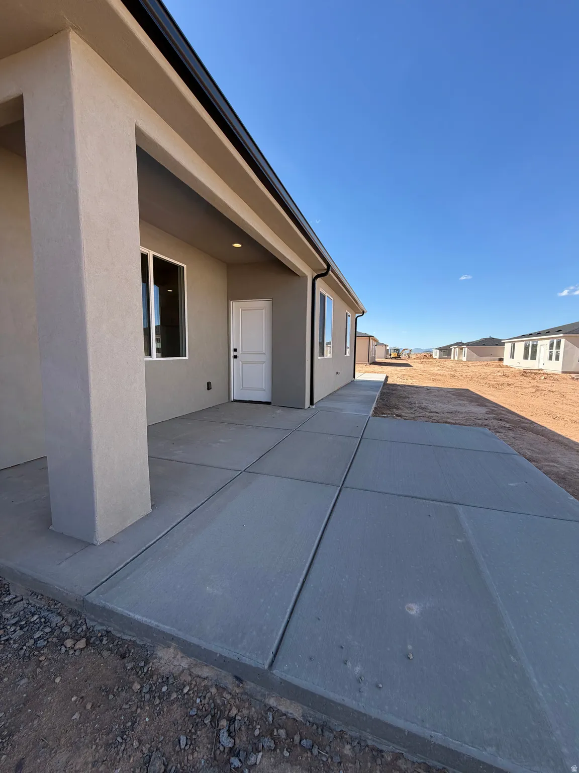 Expansive concrete patio and walkway featuring a stucco exterior, recessed lighting, and a durable black gutter system
