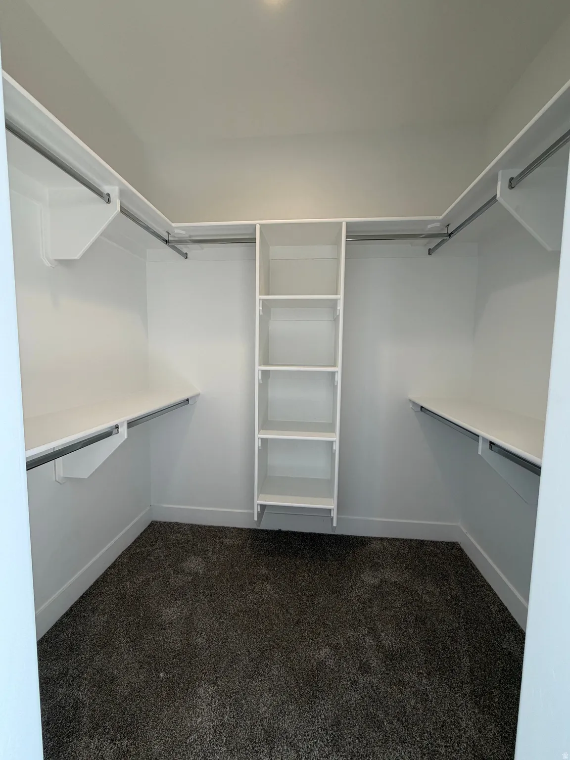 Spacious closet featuring white built-in shelving, hanging rods, and dark gray carpet flooring