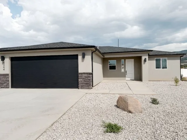 Stucco exterior featuring stacked stone accents, a dark shingle roof, a black garage door, and a concrete driveway