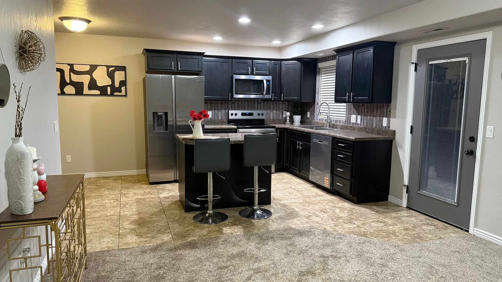 Kitchen featuring dark cabinets, appliances with stainless steel finishes, a center island, light tile patterned flooring, and a kitchen bar