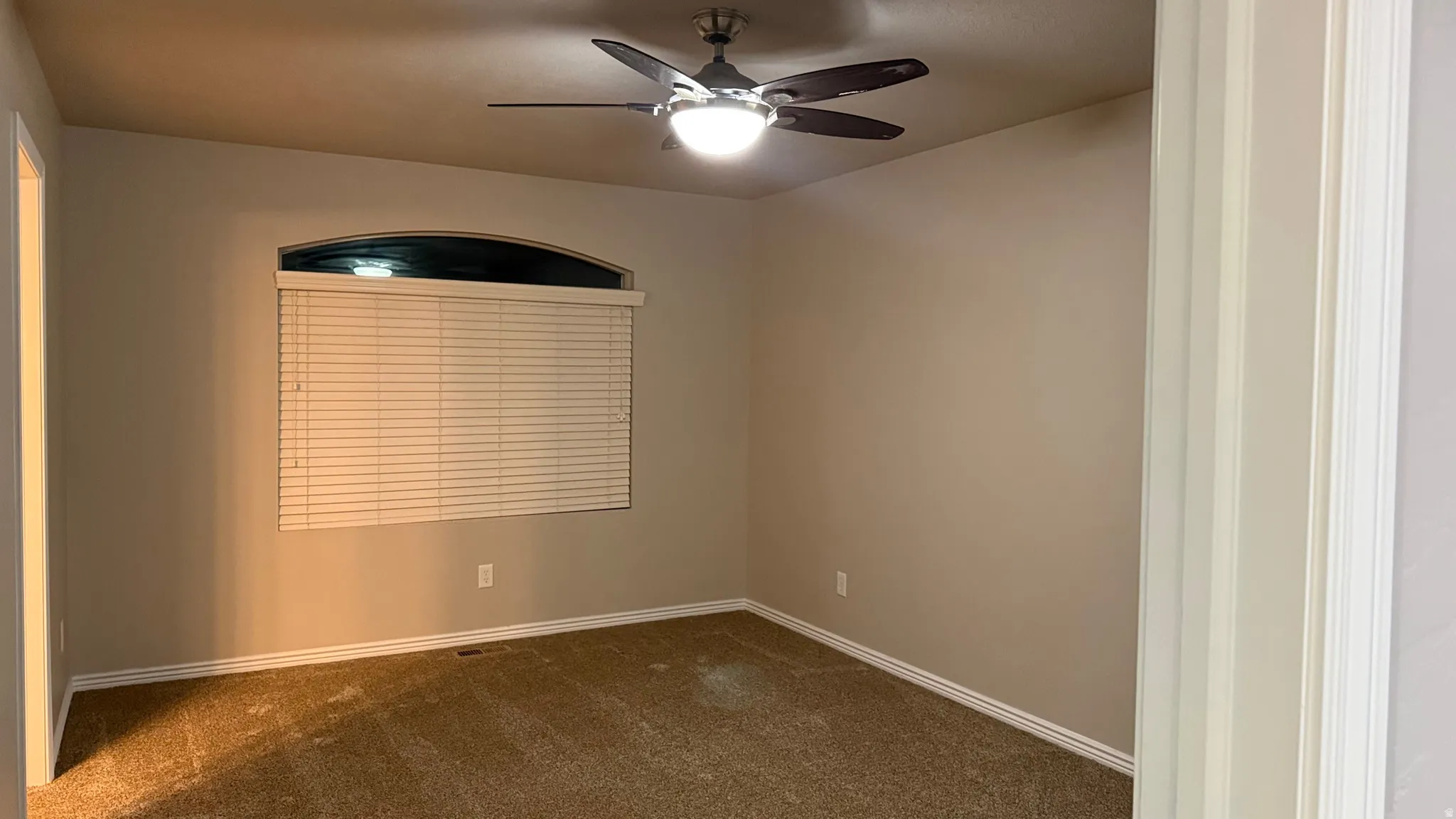 Empty room featuring dark colored carpet and a ceiling fan