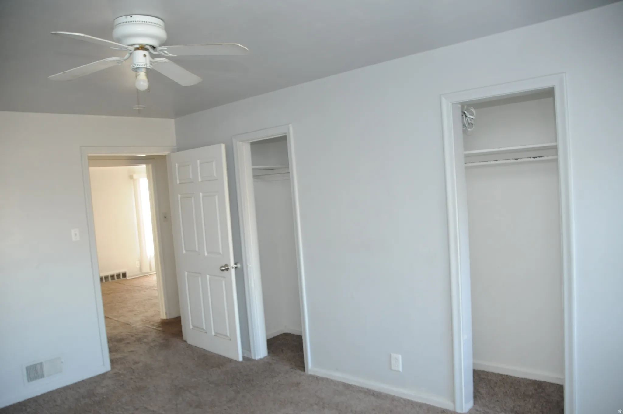 Unfurnished bedroom with carpet, two closets, and a ceiling fan
