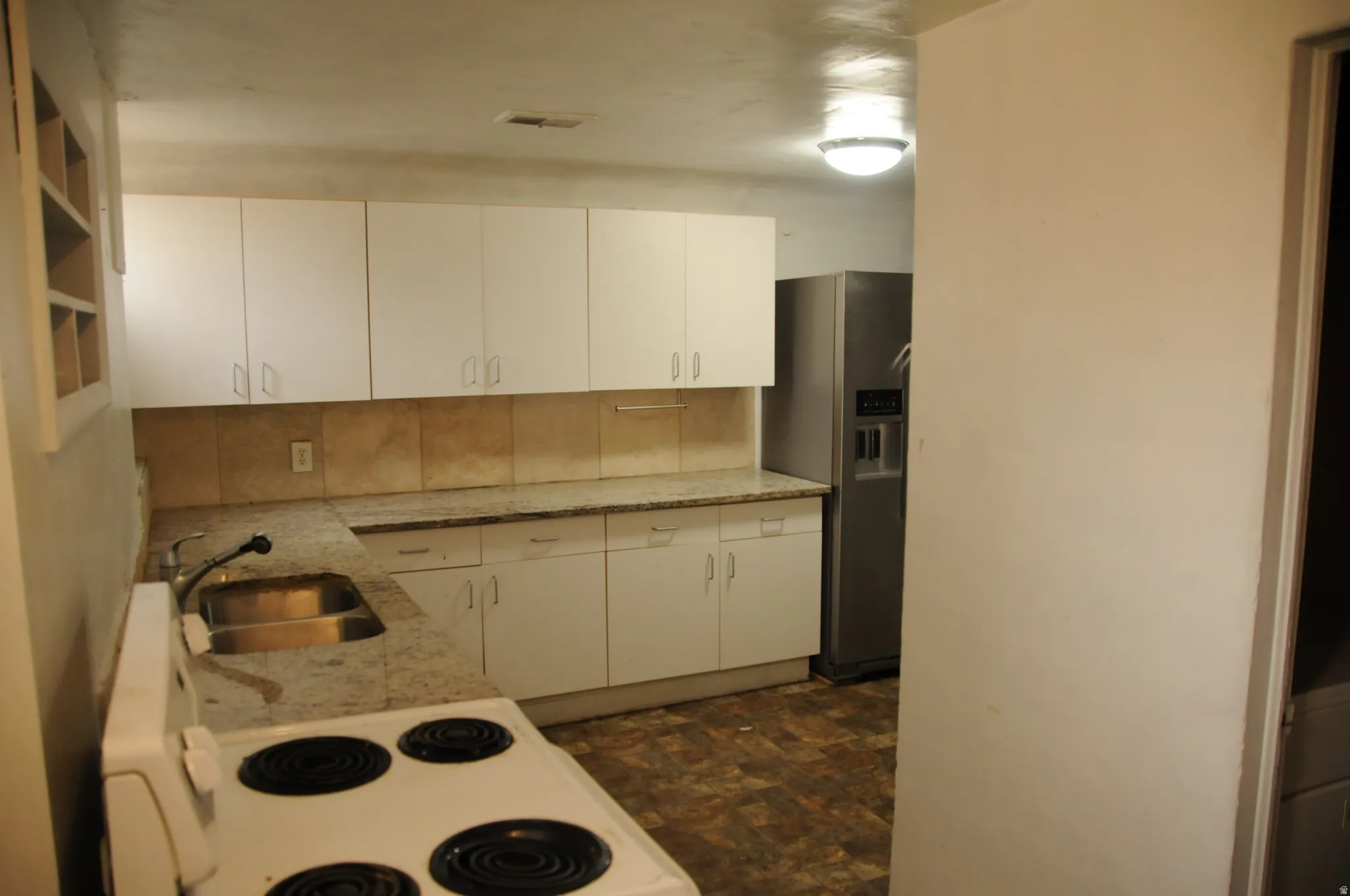 Kitchen with white cabinetry, electric range, stainless steel refrigerator with ice dispenser, and light stone counters