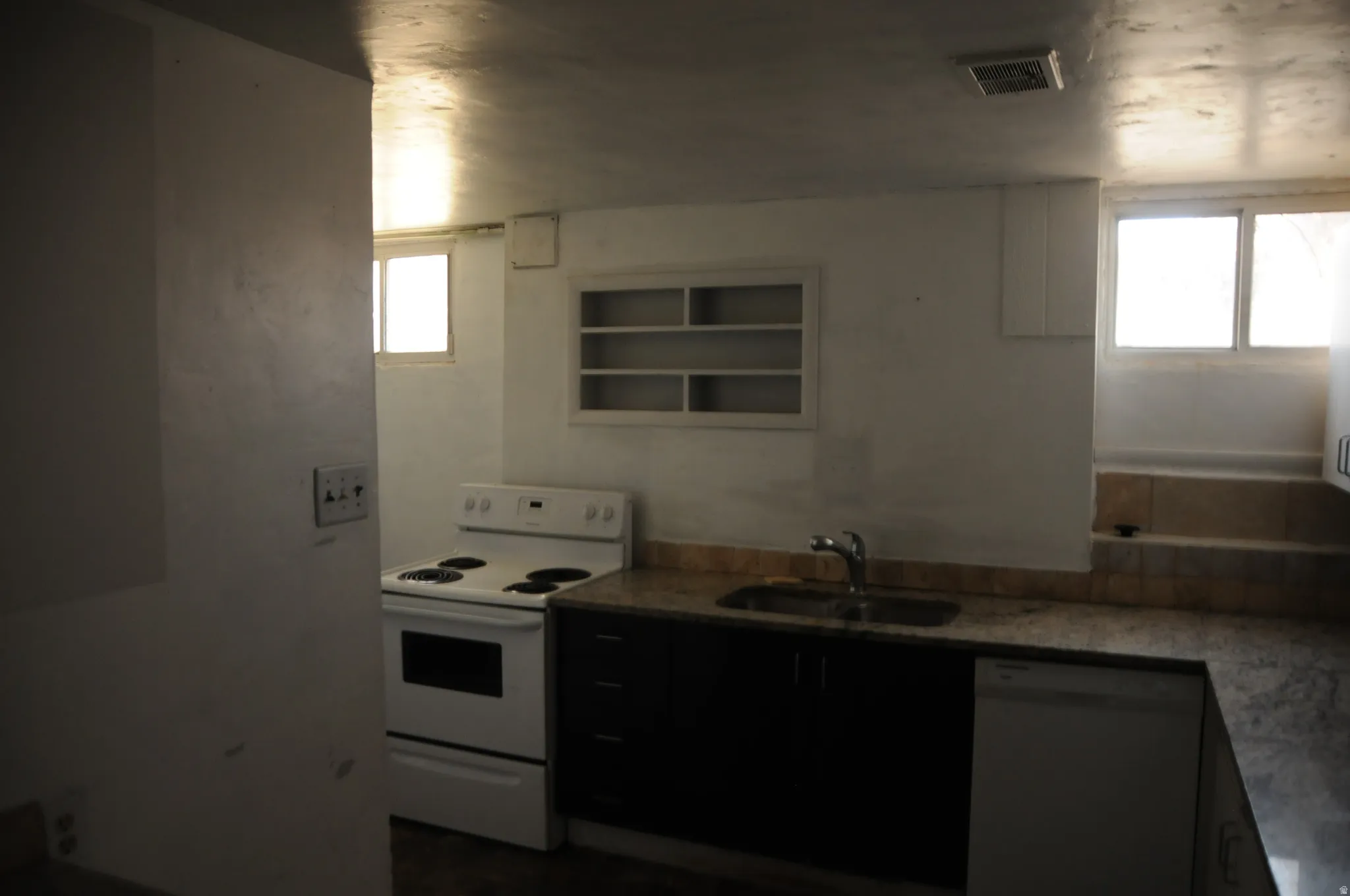 Kitchen with electric stove, stainless steel dishwasher, open shelves, and light stone countertops