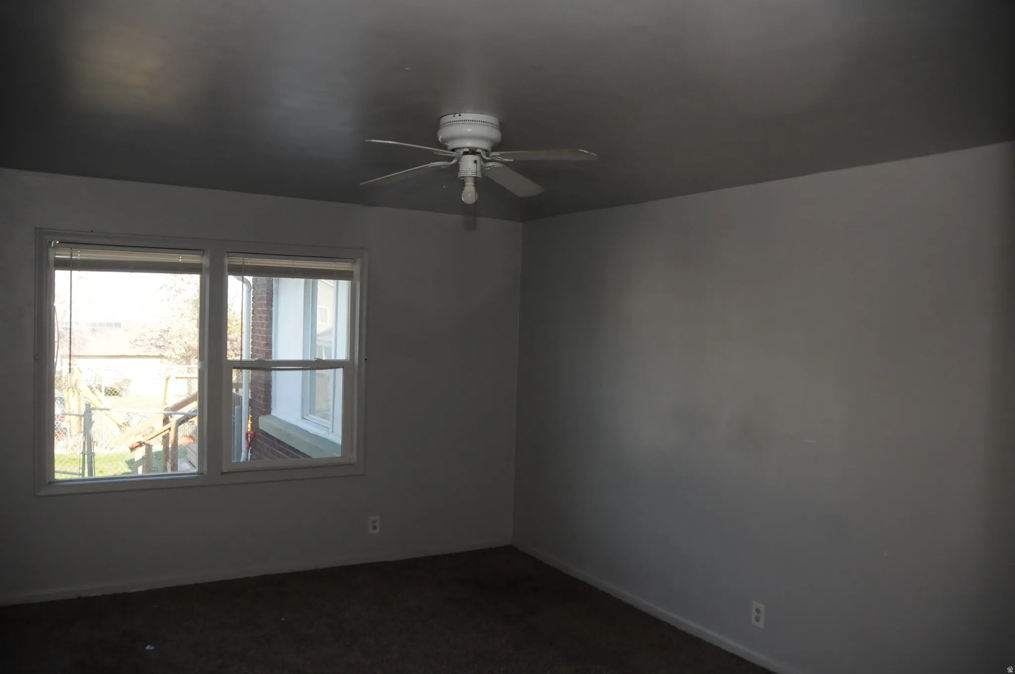 Empty room with a ceiling fan and dark carpet