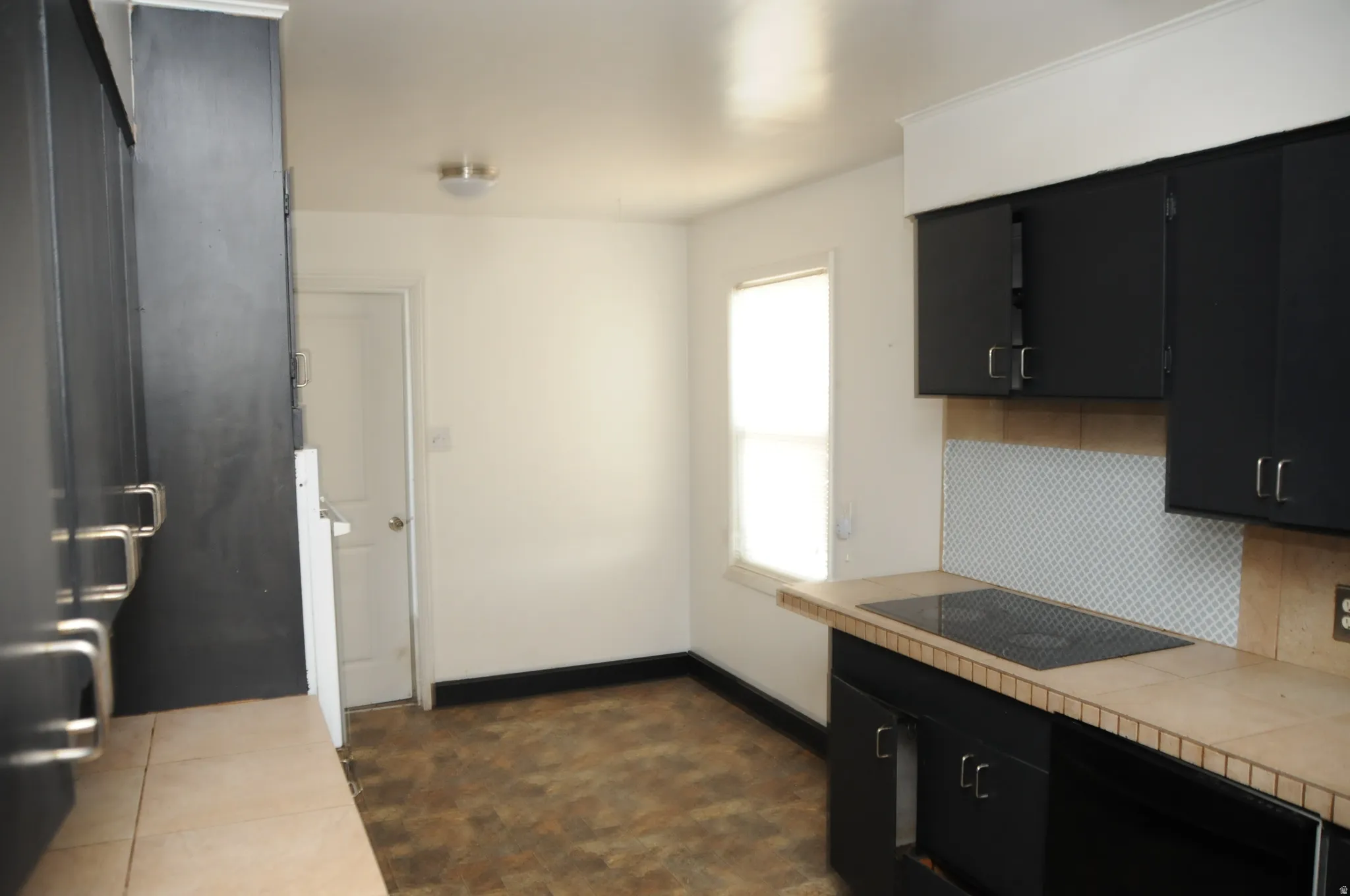 Kitchen featuring dark cabinets, tile counters, black appliances, and tasteful backsplash