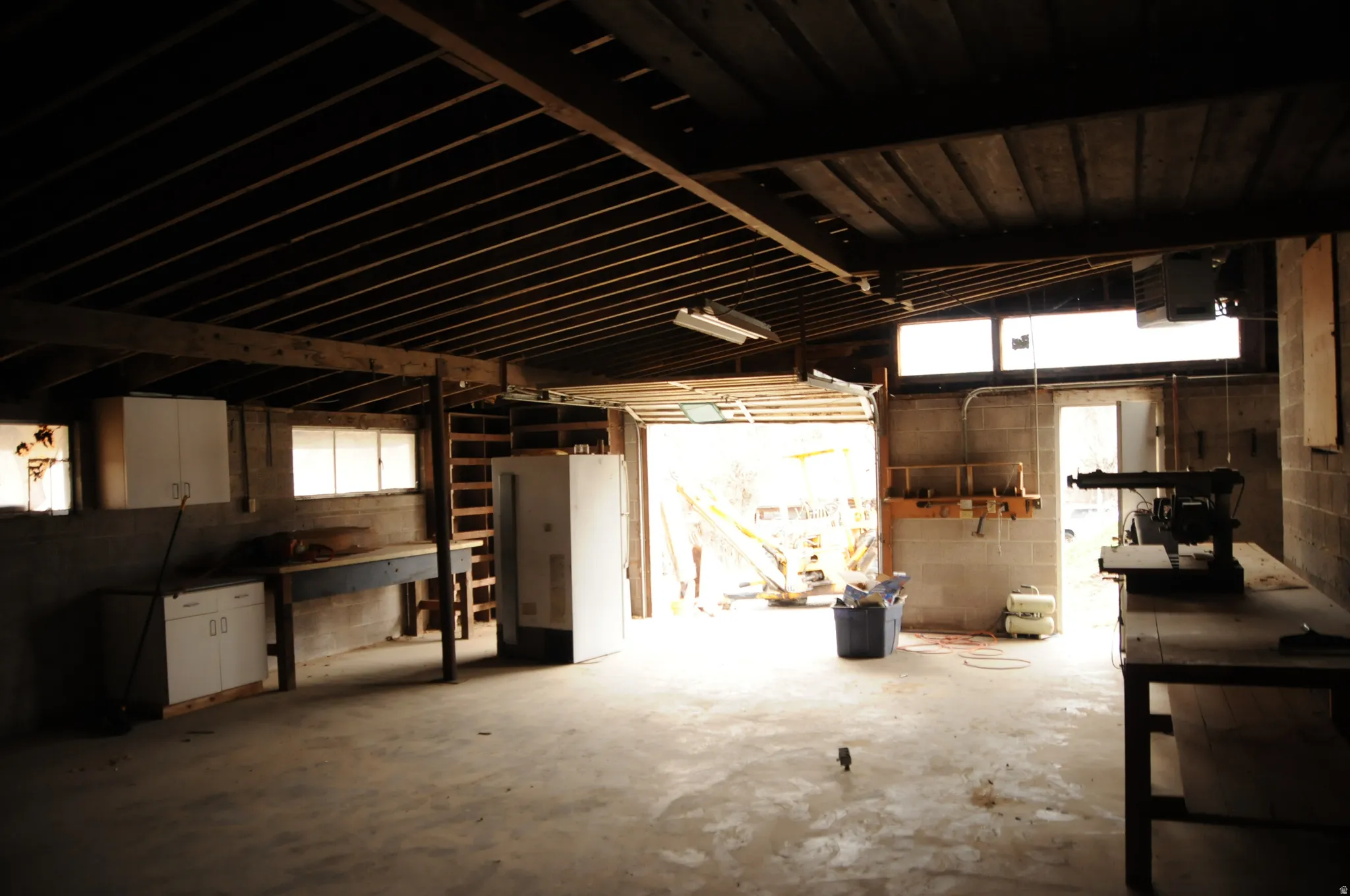 Misc room with concrete block wall, a heating unit, lofted ceiling, unfinished concrete floors, and a garage