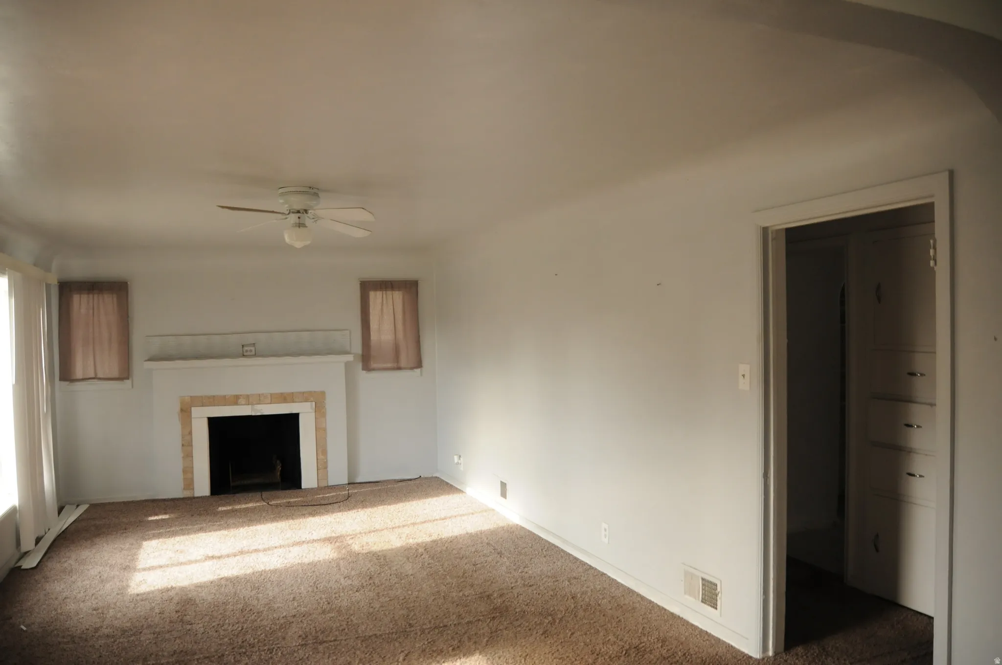 Unfurnished living room with carpet flooring, a fireplace, a ceiling fan, and baseboard heating