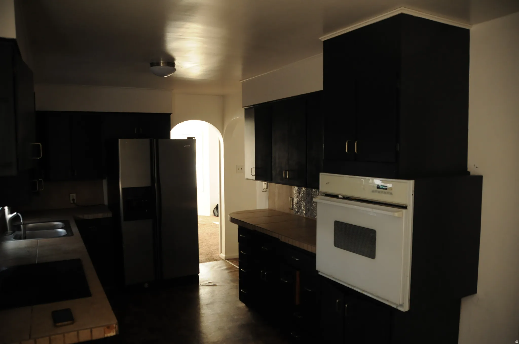 Kitchen featuring dark cabinets, arched walkways, stovetop, and oven