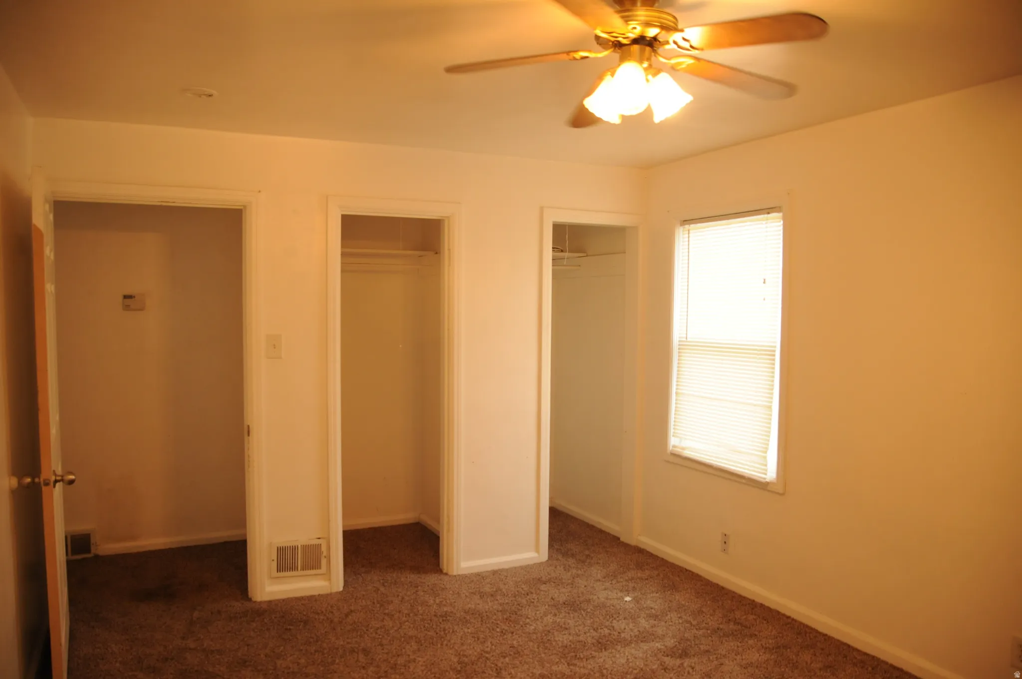Unfurnished bedroom with multiple closets, dark carpet, and a ceiling fan