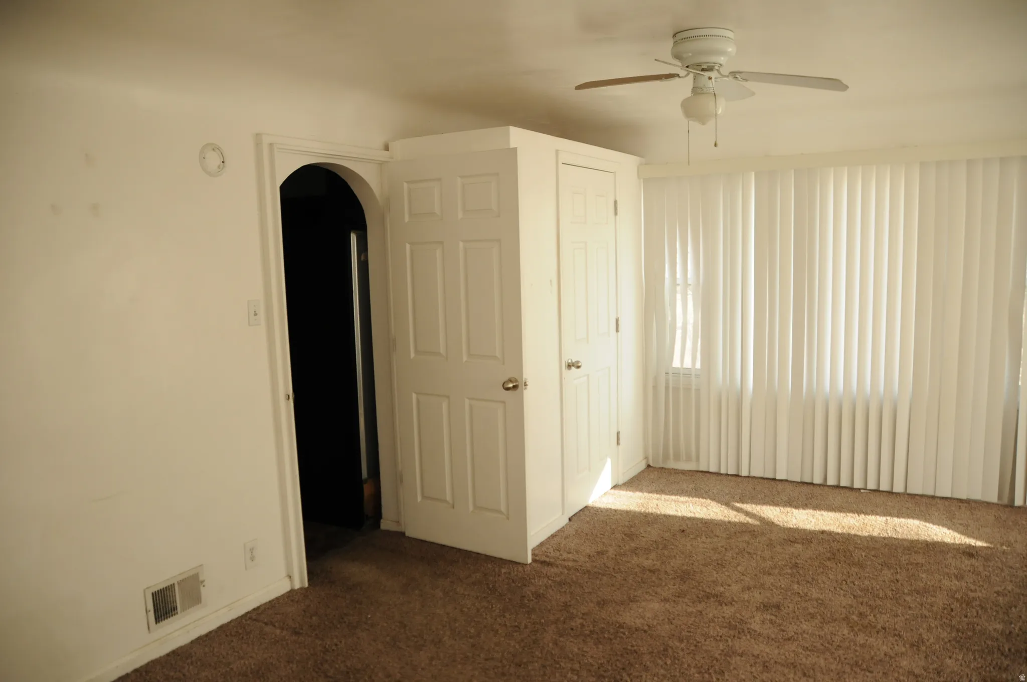 Unfurnished bedroom featuring dark carpet, arched walkways, and a ceiling fan