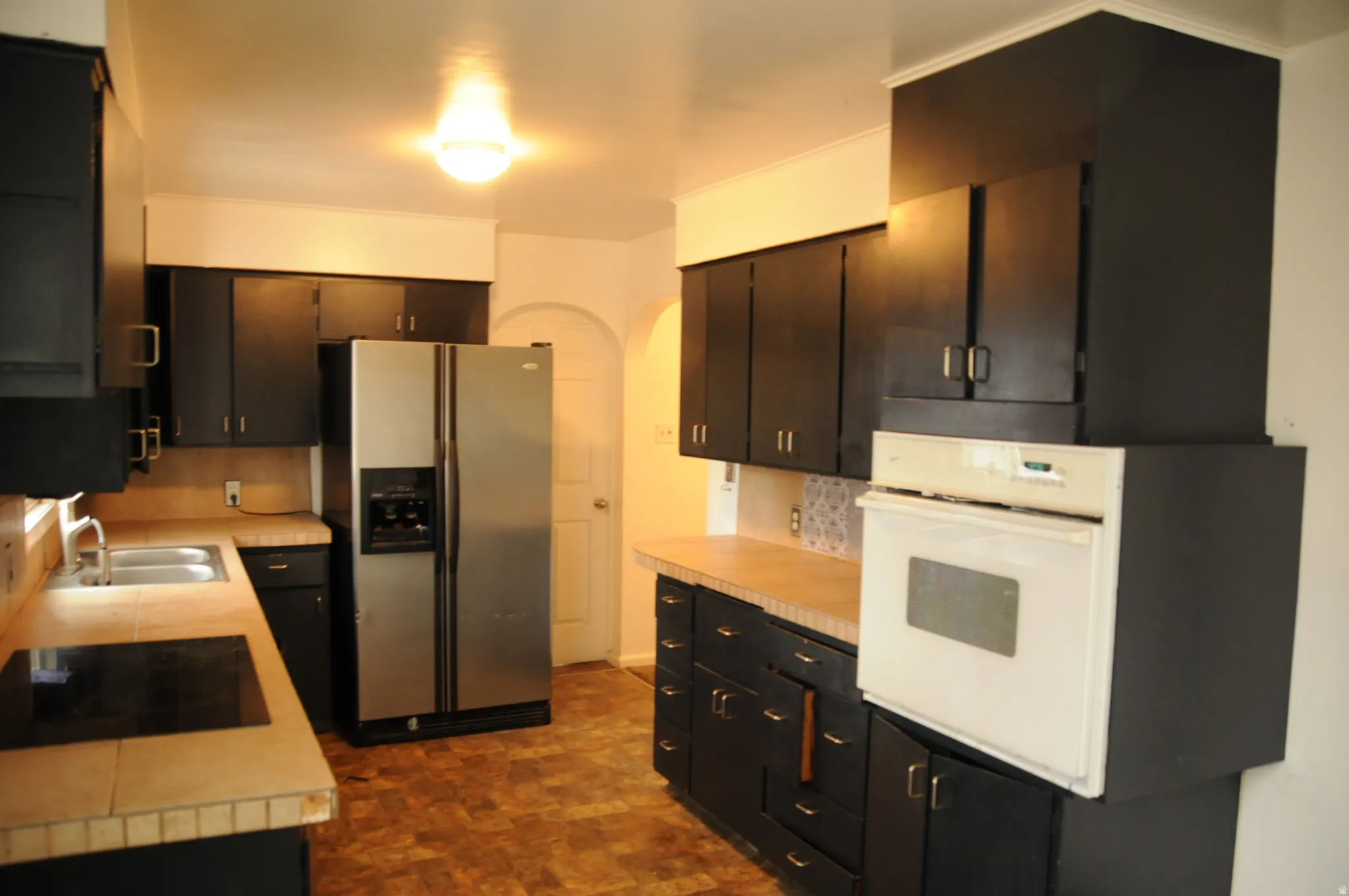 Kitchen with arched walkways, stainless steel refrigerator with ice dispenser, oven, light countertops, and black electric stovetop