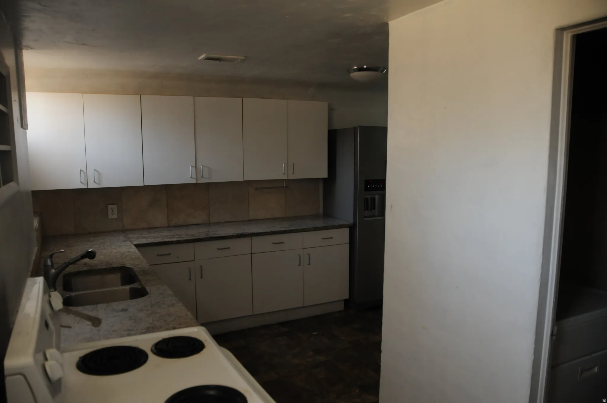 Kitchen with white electric range oven, white cabinets, stainless steel refrigerator with ice dispenser, light stone counters, and dark flooring